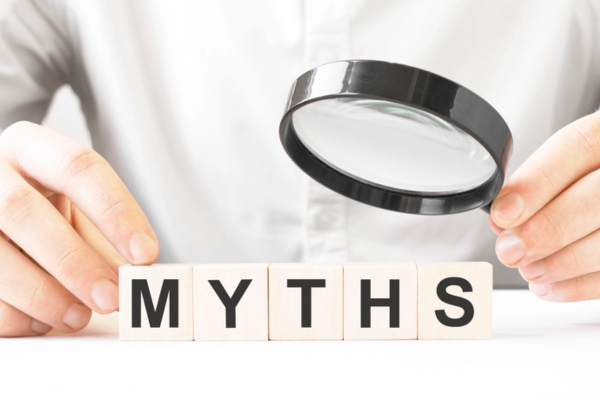 businessman holding a magnifying glass on top of the word myths